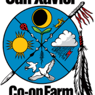 A group of people stands in a green field with a mountainous backdrop under a clear blue sky.