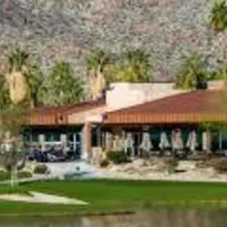 A lush golf course with palm trees and mountains in the background under a clear blue sky at Indian Canyons Golf Resort.