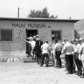 The image shows the entrance to Malki Museum with a wooden sign and surrounding native plants in Temalpakh Garden, Banning, CA.