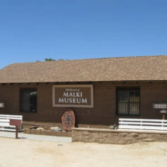 Historic building surrounded by desert plants; Malki Museum signage and Temalpakh Garden entrance visible.