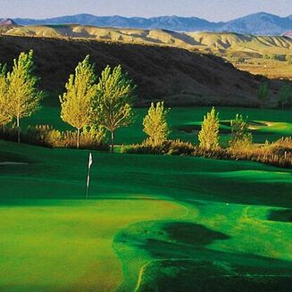 Green golf course with rolling hills, sand traps, and a backdrop of mountains under a clear blue sky at Morongo Golf Club.