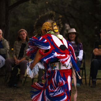 Native American dancers in vibrant regalia performing a traditional dance at a cultural festival, surrounded by colorful flags and spectators.